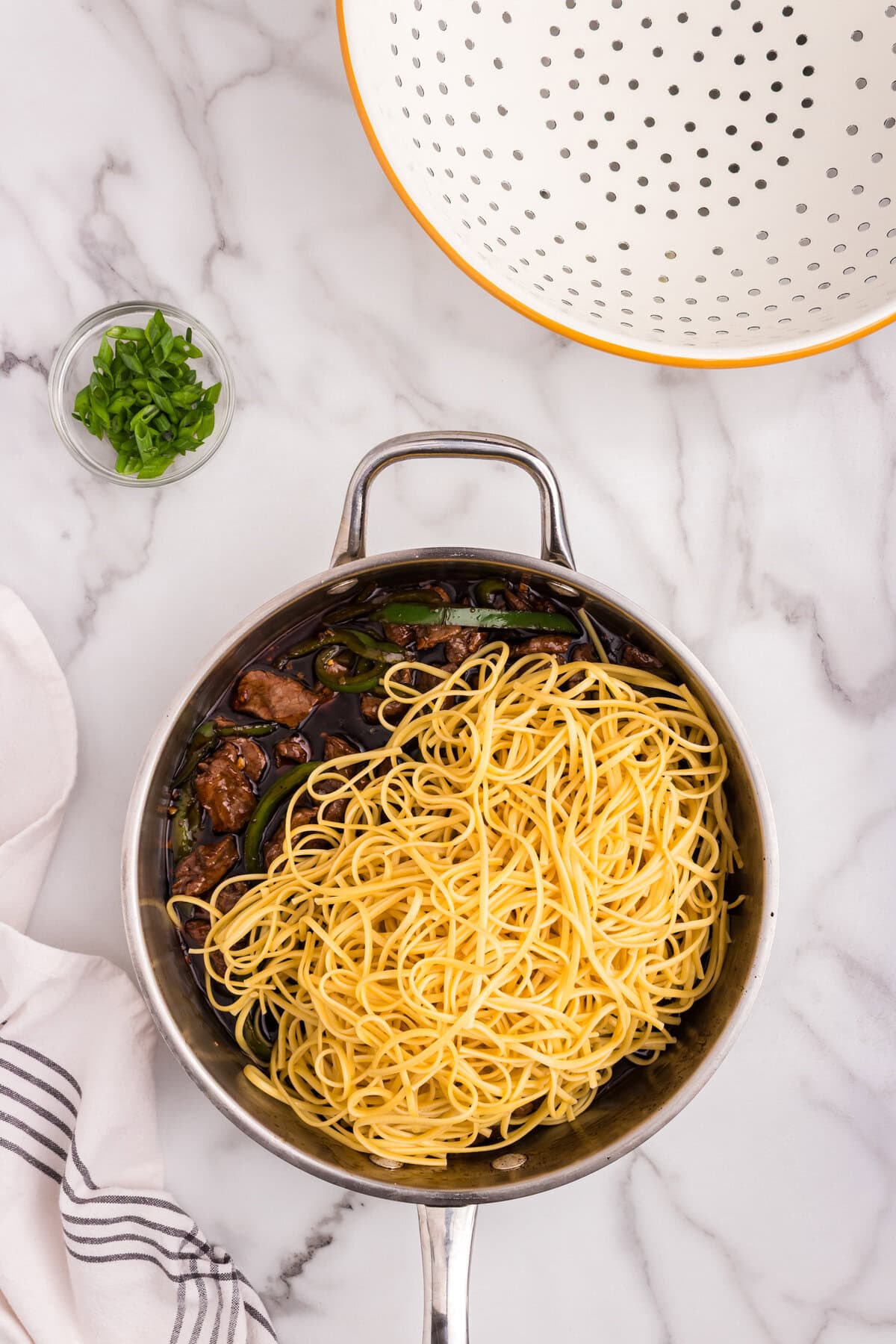 Cooked noodles added to the skillet with Mongolian beef, green peppers, and sauce, ready to be mixed.
