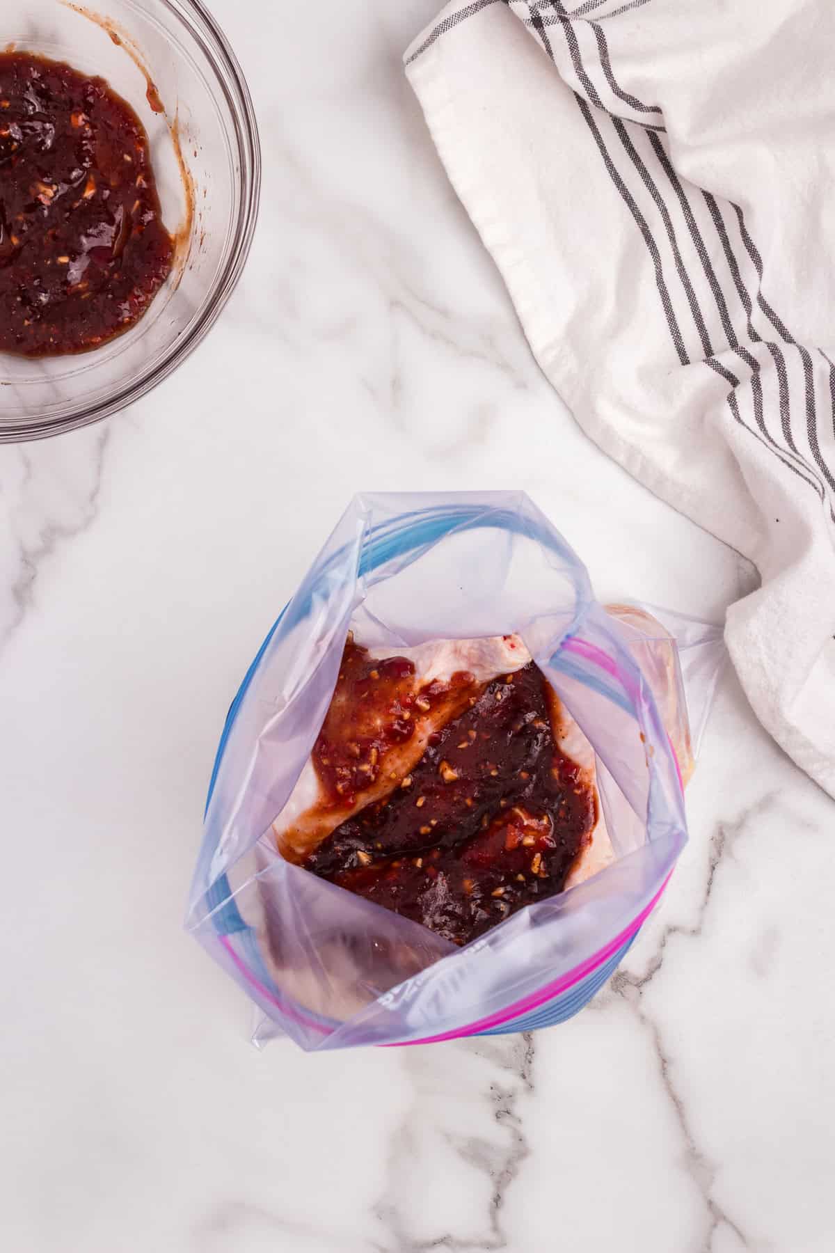 Raw chicken drumsticks placed in a zip-top bag, partially covered with the prepared BBQ marinade.