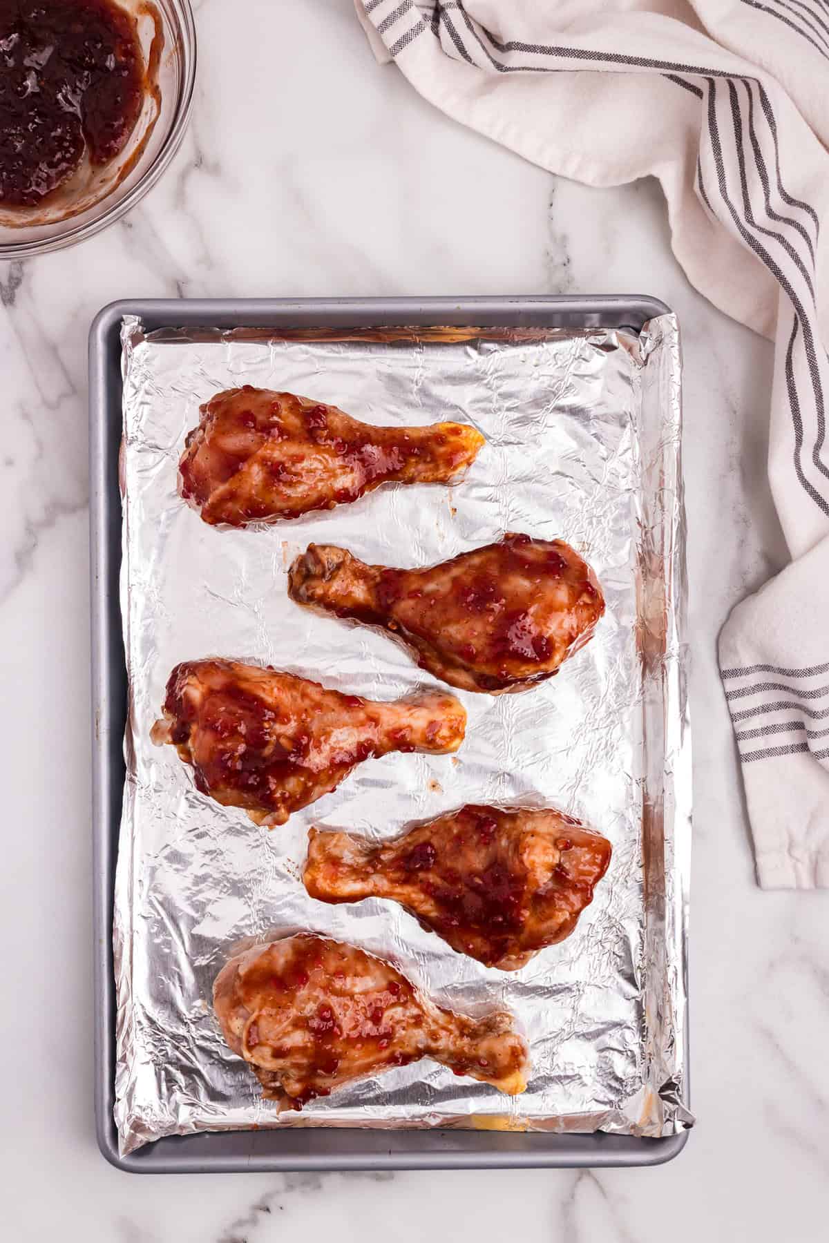 Marinated chicken drumsticks arranged on a foil-lined baking sheet, ready for the oven.