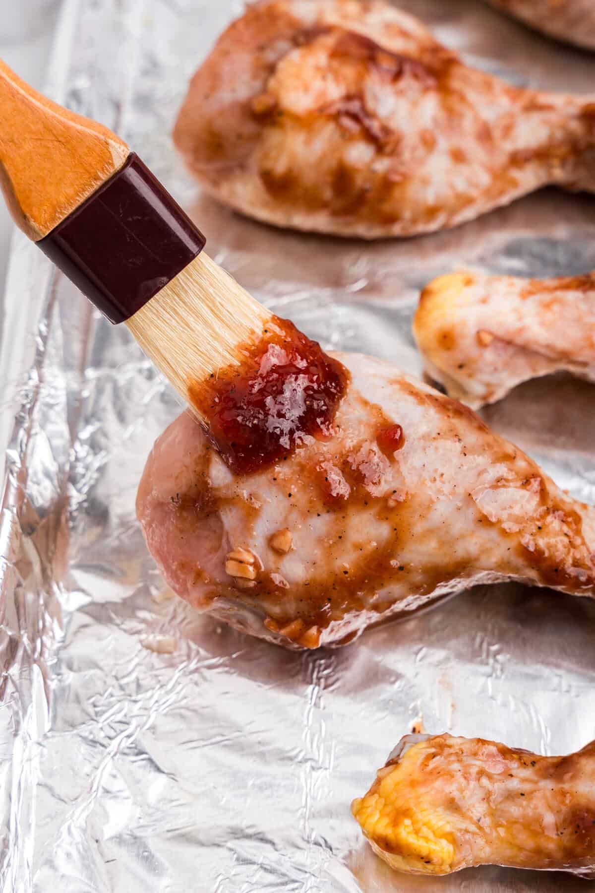 A close-up of a brush applying extra marinade to a chicken drumstick on the baking sheet before or during baking.