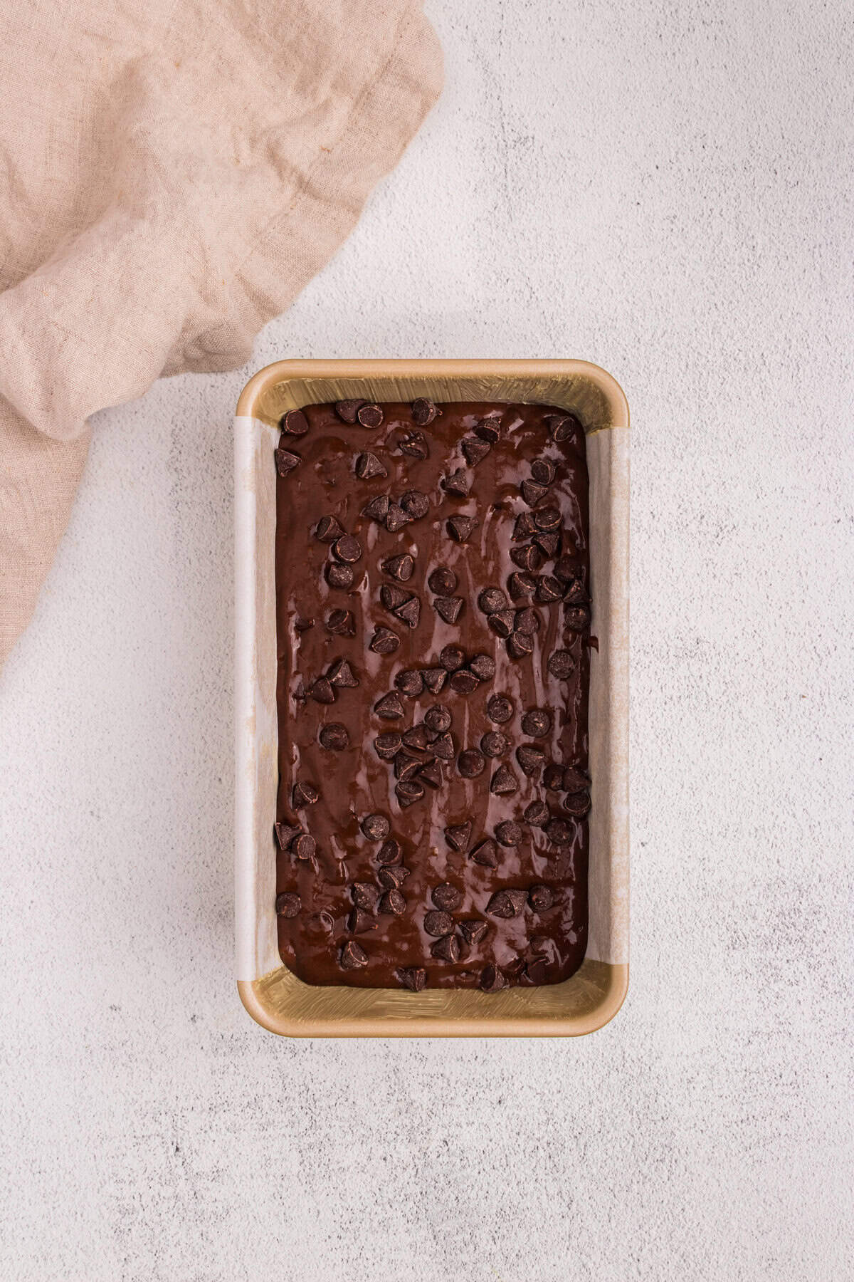 A loaf pan filled with smooth chocolate batter, topped generously with chocolate chips, ready to go into the oven.