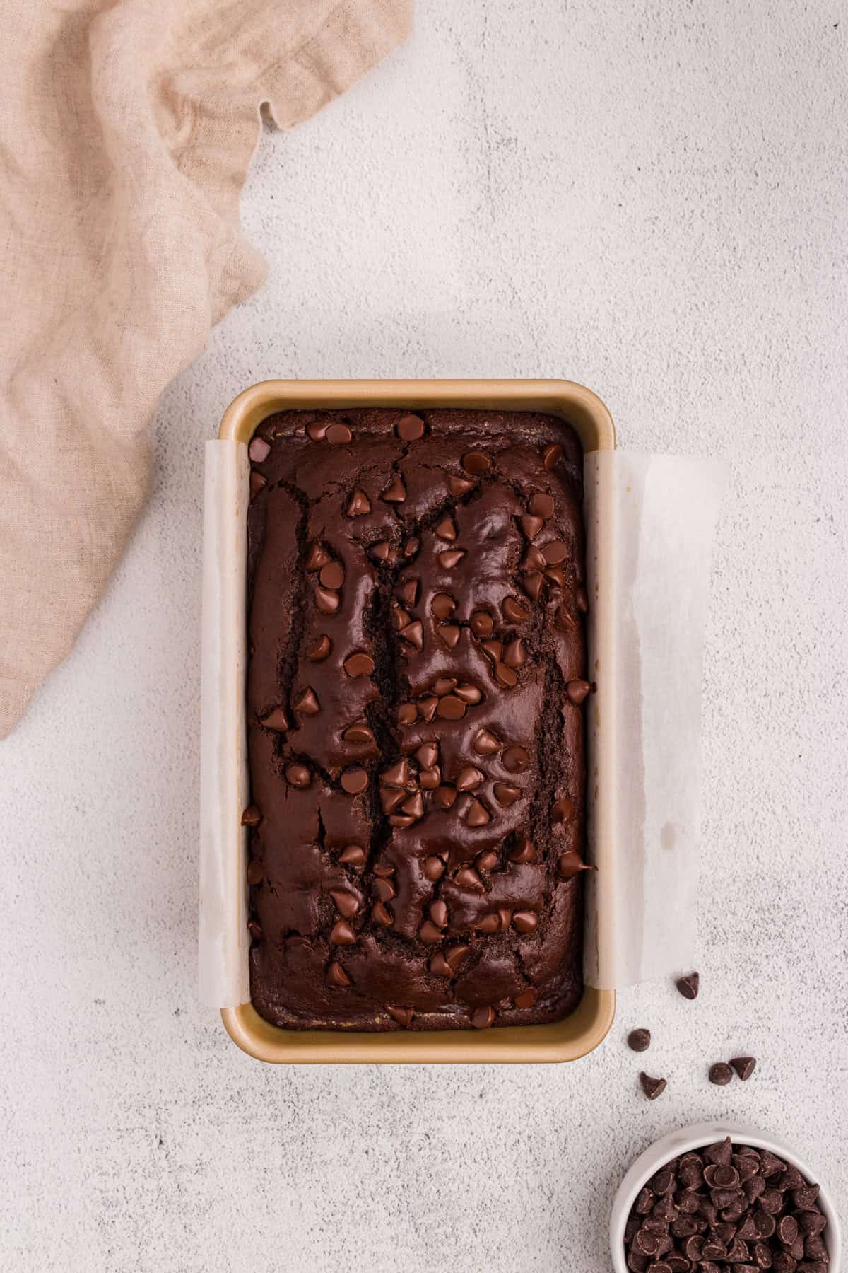 Freshly baked chocolate bread still in the loaf pan, with a cracked top and melty chocolate chips throughout the surface.