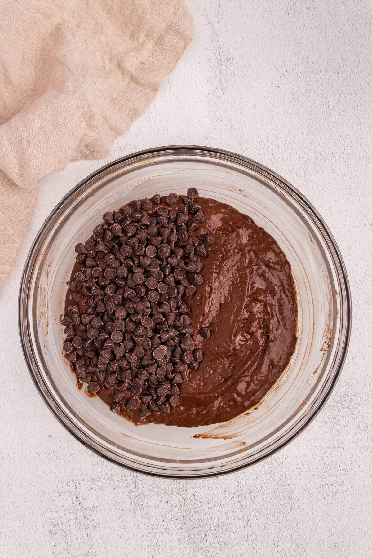 A large portion of chocolate chips has been added to one side of the chocolate batter in the bowl.