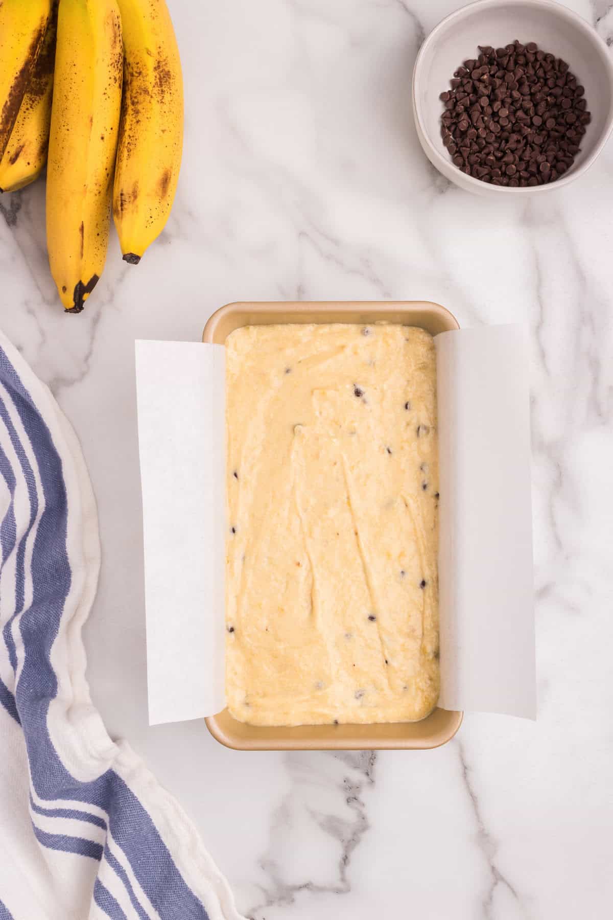 The chocolate chip banana bread batter has been poured into the parchment-lined loaf pan, spread evenly and ready for baking.