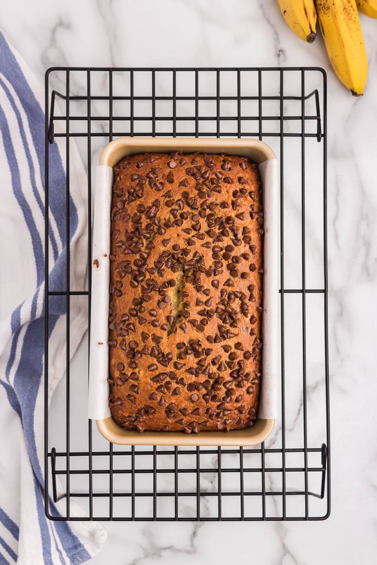 The chocolate chip banana bread is fully baked and golden brown, still in the loaf pan and resting on a wire cooling rack.