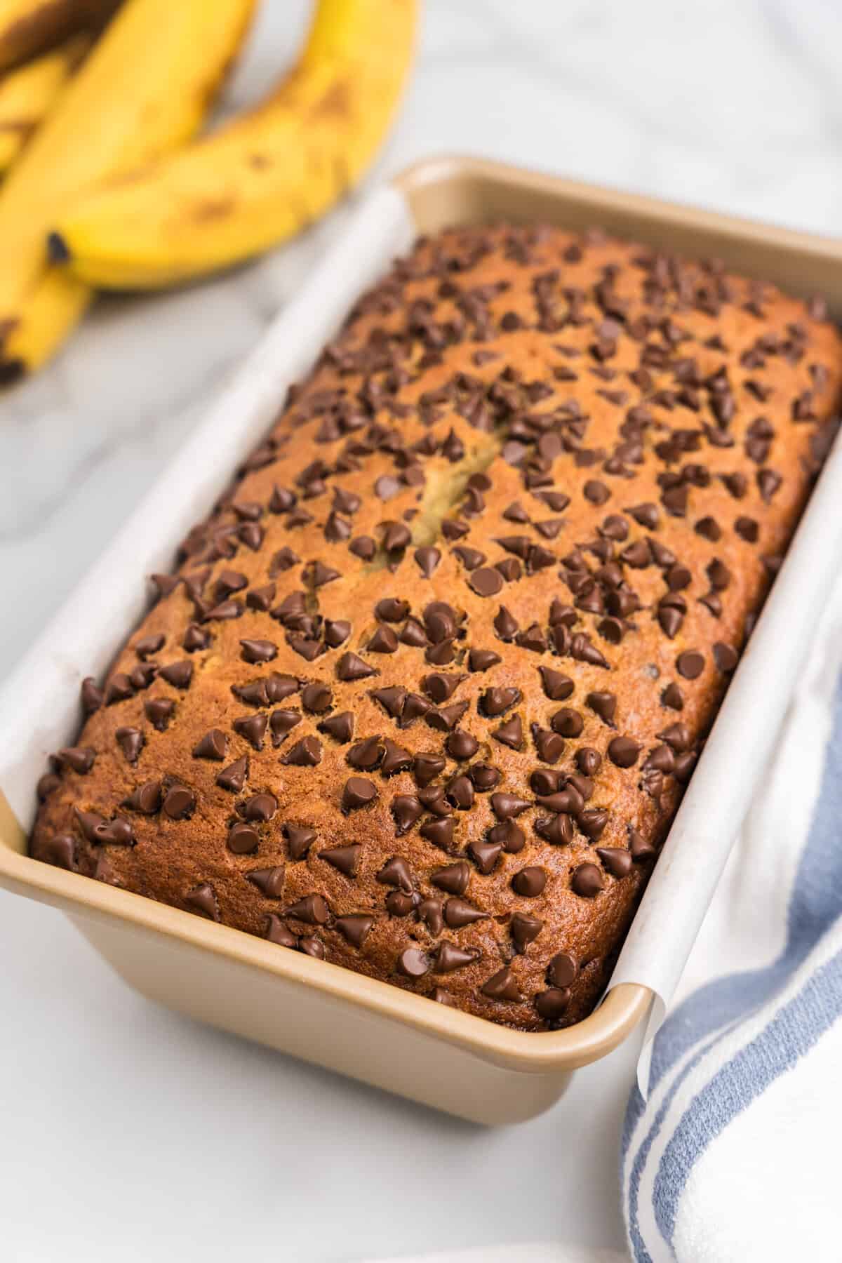 A closer angled view of the freshly baked chocolate chip banana bread still in the pan, showing the crisp, golden top covered with melted chocolate chips.