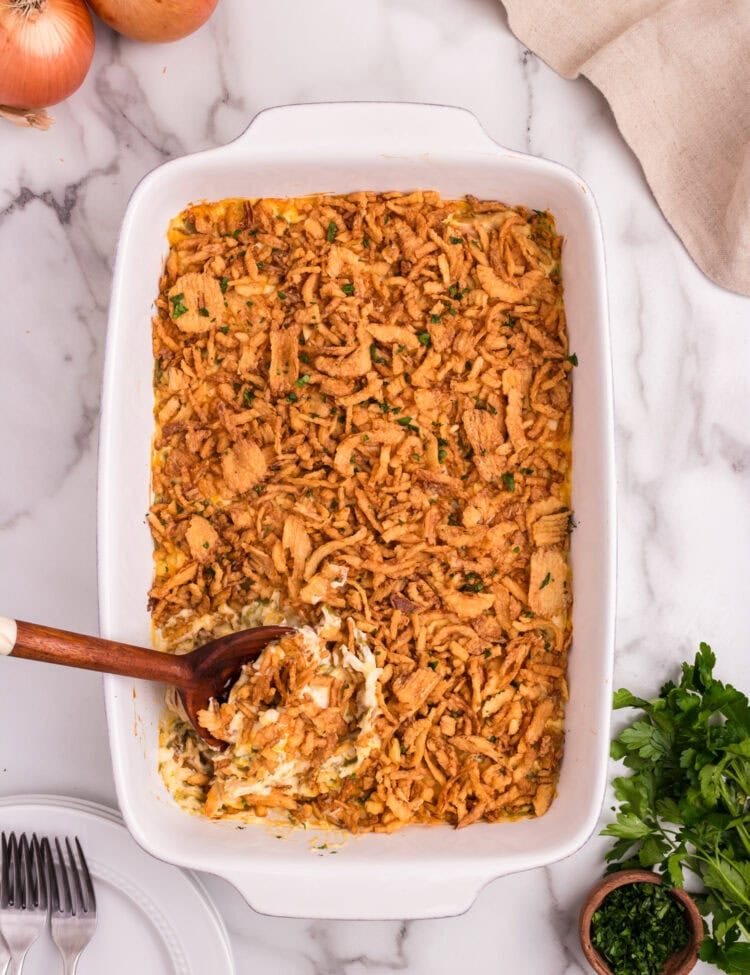 A wooden spoon scooping into the crispy-topped casserole, revealing the creamy chicken and green bean filling underneath.