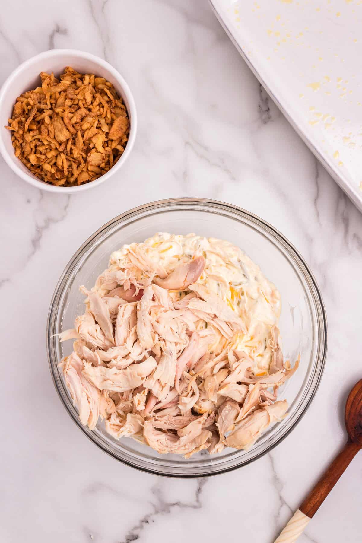 Shredded chicken just added on top of the creamy mixture in the glass bowl, ready to be stirred in.