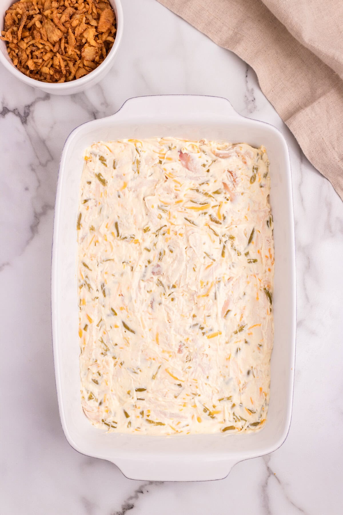 The creamy chicken and green bean mixture evenly spread in a white baking dish, ready for baking.