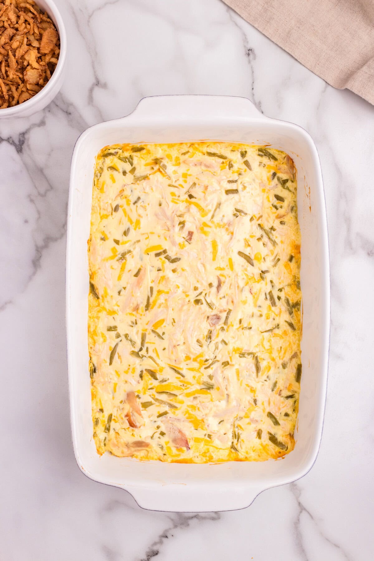 Baked casserole in the dish showing a golden, set top with visible green bean and cheese strands.