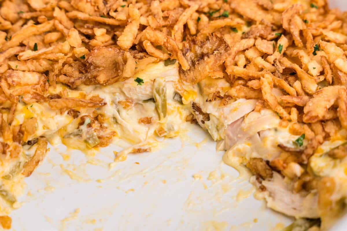 Close-up view of the casserole's inside layers, displaying shredded chicken, green beans, cheese, and creamy sauce beneath the crispy onion topping.