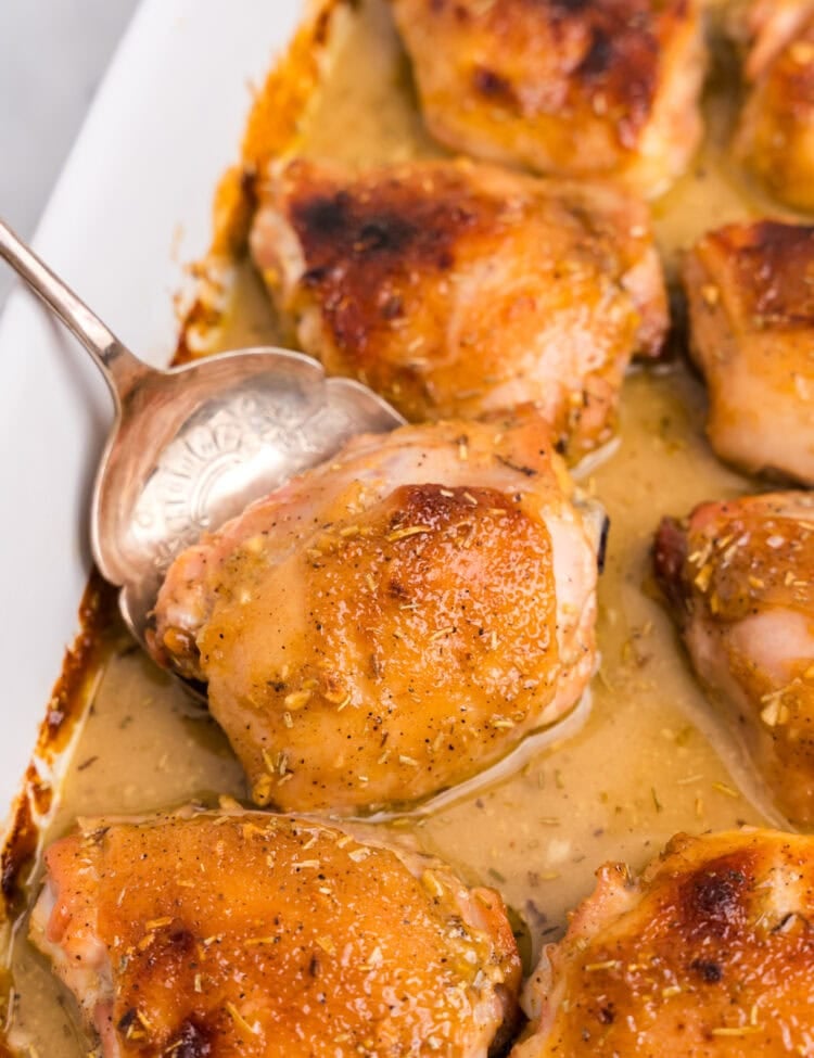 Spoon is taking a chicken thigh coated in honey mustard sauce out of a casserole dish.