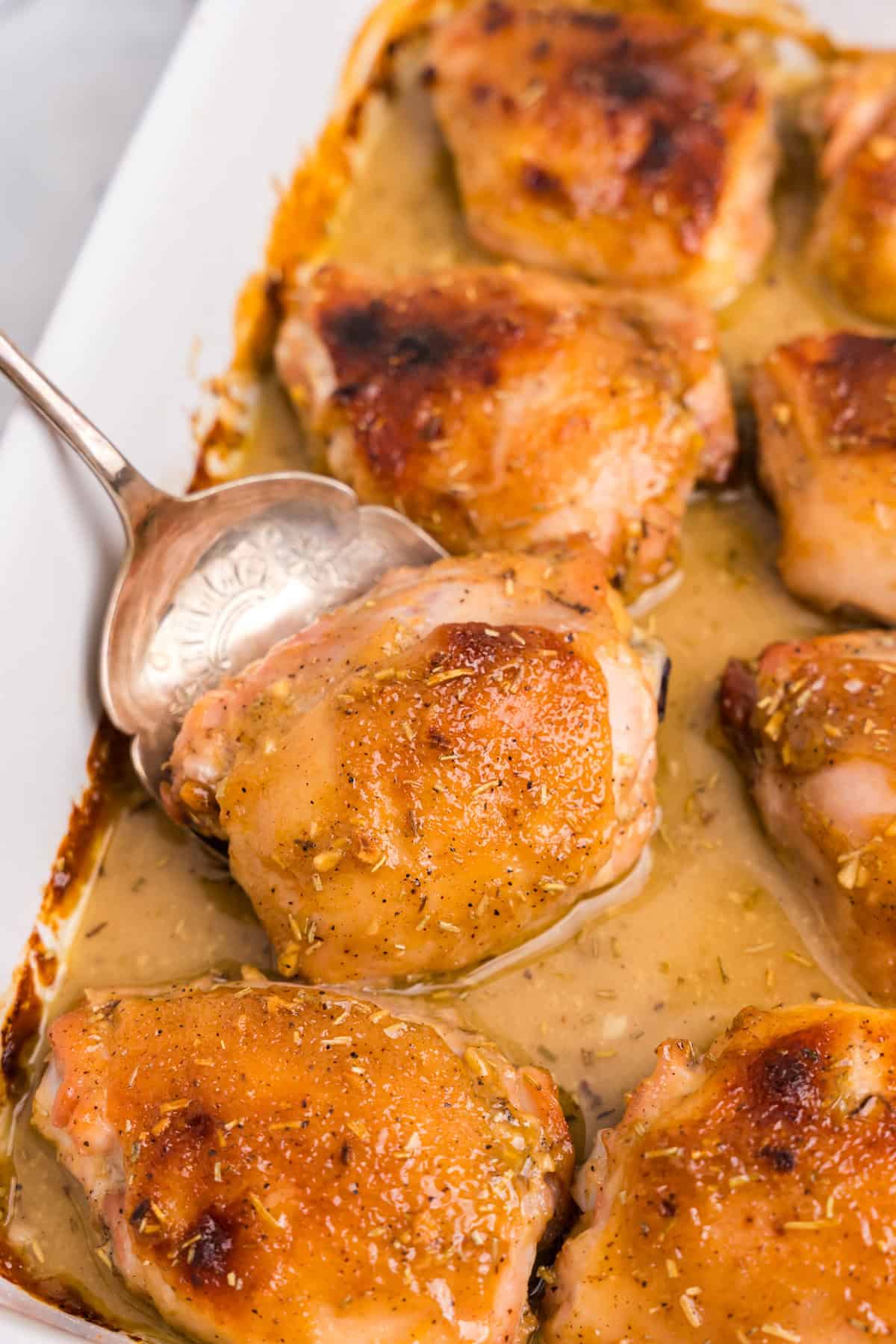 Spoon is taking a chicken thigh coated in honey mustard sauce out of a casserole dish.