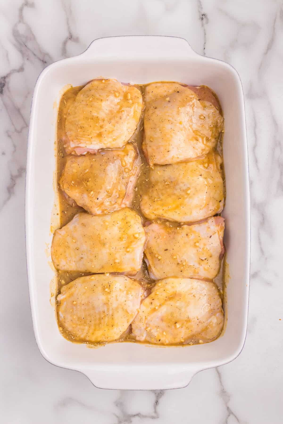 Raw chicken thighs coated with honey mustard sauce in a baking dish, ready to bake.