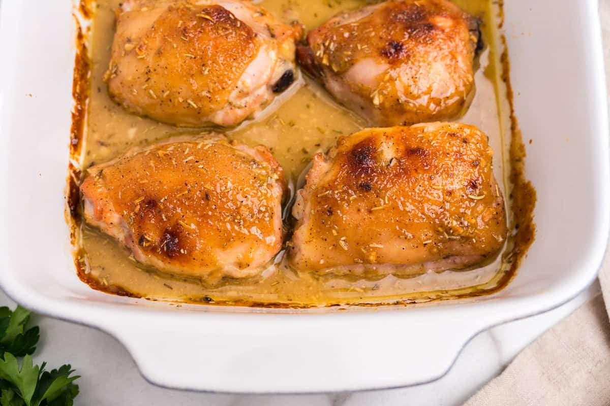 Golden-brown baked chicken thighs in a honey mustard sauce, resting in a white baking dish.
