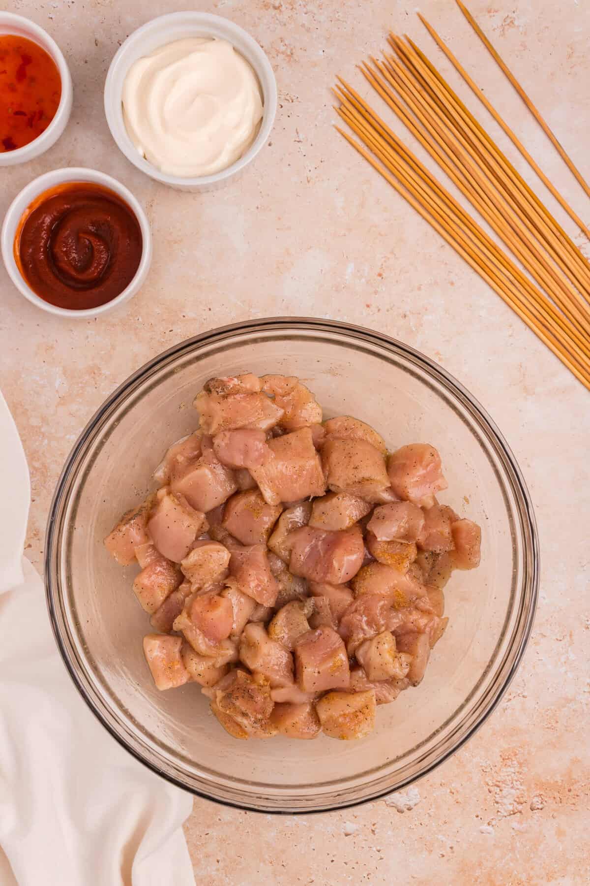 The chicken in the bowl has been fully mixed and coated with the seasonings, ready for skewering. The surrounding ingredients and skewers remain in place.