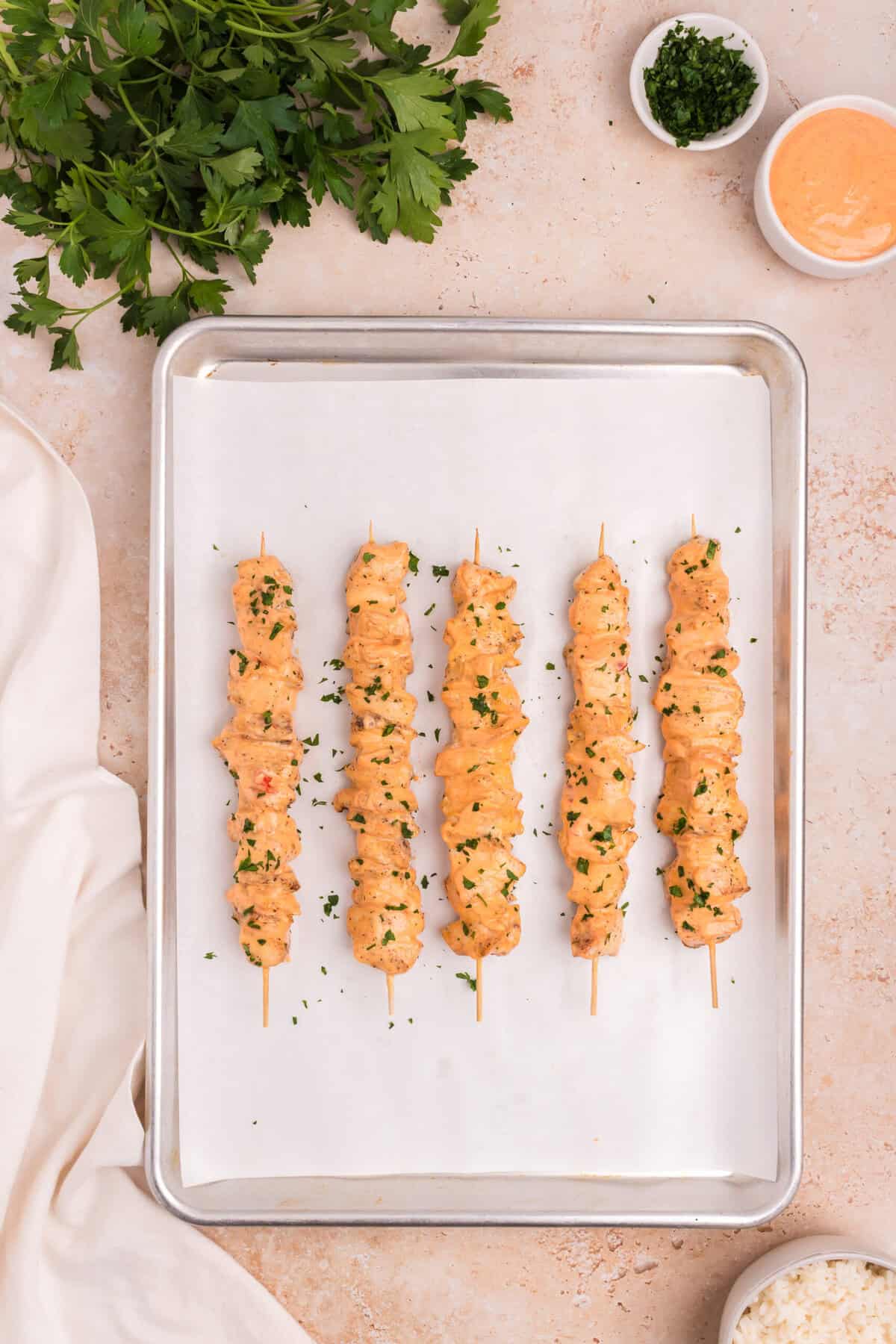 The cooked chicken skewers have been brushed with the spicy mayo sauce and sprinkled with chopped parsley, presented on a tray ready to serve with dipping sauce and rice on the side.