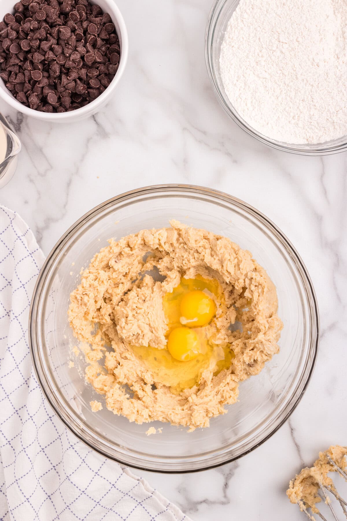 Two eggs are added to the creamed butter and sugar mixture in a glass bowl. The ingredients are partially mixed.