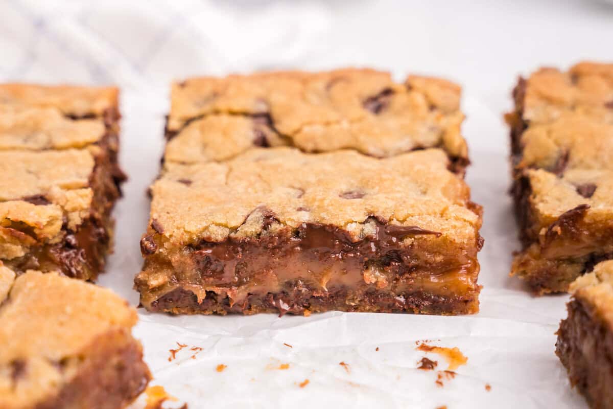A close-up of multiple sliced bars arranged on parchment paper, highlighting the melty chocolate and caramel center.