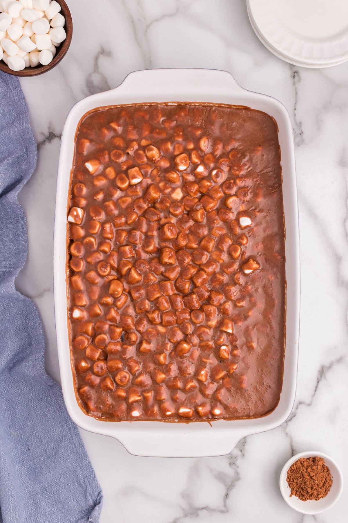 Fully assembled Mississippi Mud Cake with melted marshmallows and chocolate glaze forming a gooey topping layer in a baking dish.