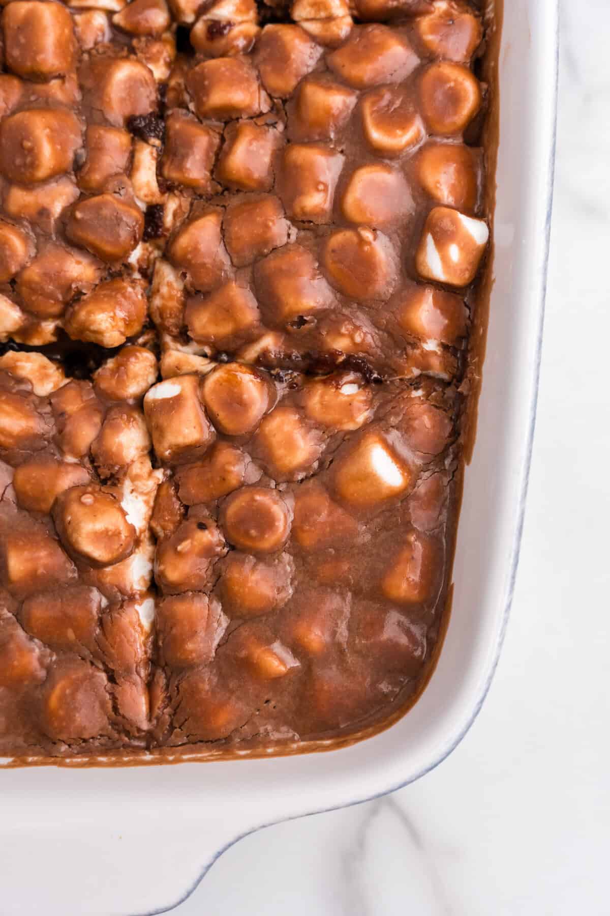 Close-up view of the cake surface showing melted and slightly toasted marshmallows coated in rich chocolate glaze, with visible cuts in the cake.