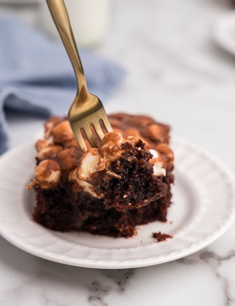 Fork lifting a moist bite of Mississippi Mud Cake from a serving on a white plate, showing the gooey marshmallow and chocolate interior.