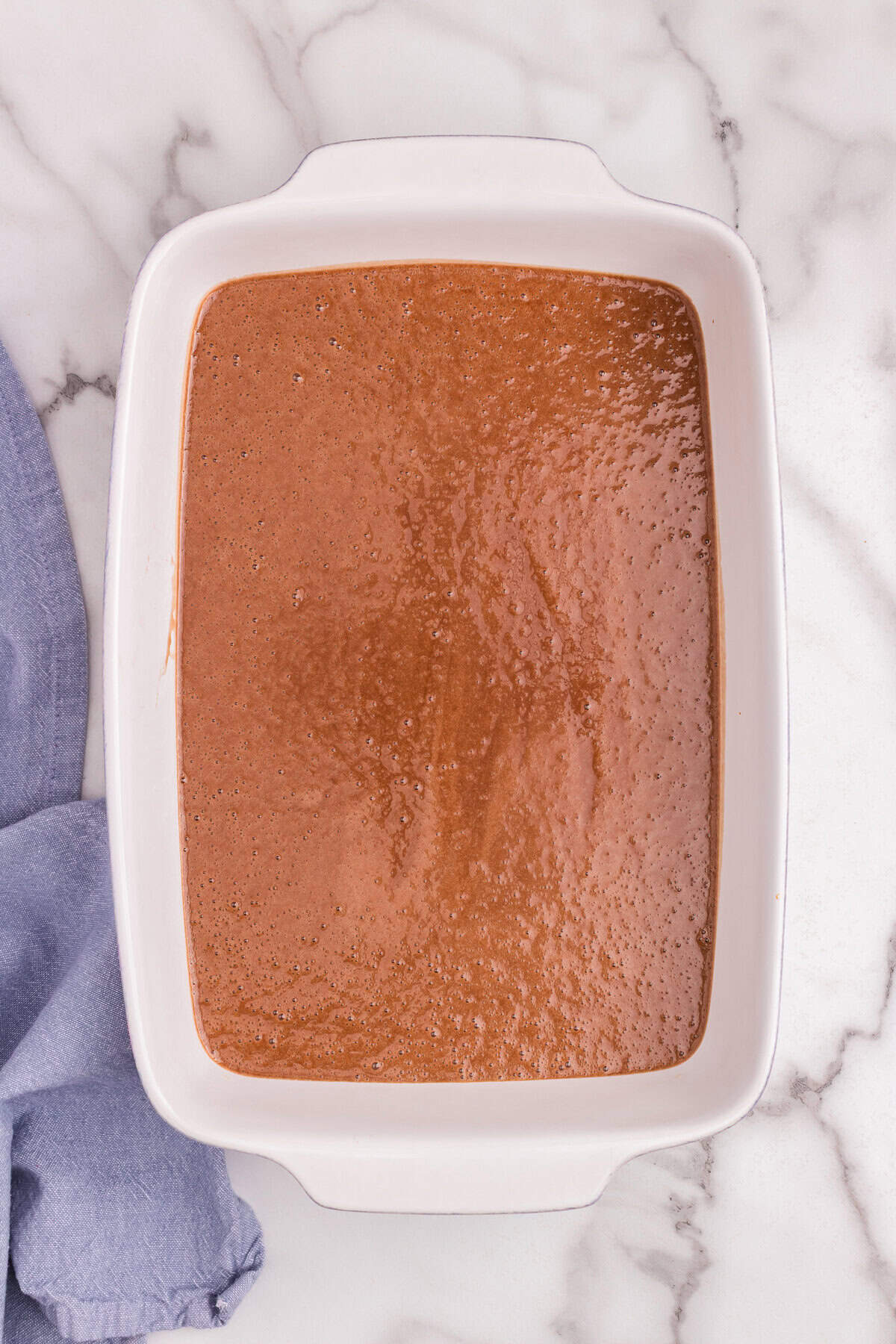 Finished chocolate cake batter evenly spread into a white rectangular baking dish