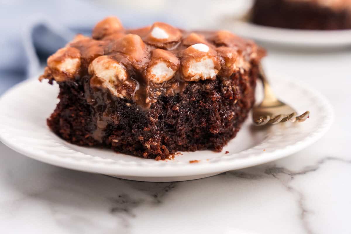 Side view of a square slice of Mississippi Mud Cake on a white plate, showcasing the dense chocolate cake base and melted marshmallow-chocolate topping.