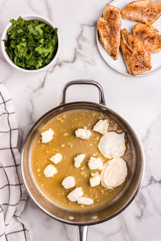Softened cream cheese, sour cream, and minced garlic beginning to melt into a broth in a stainless steel skillet, prepped to become the sauce base.