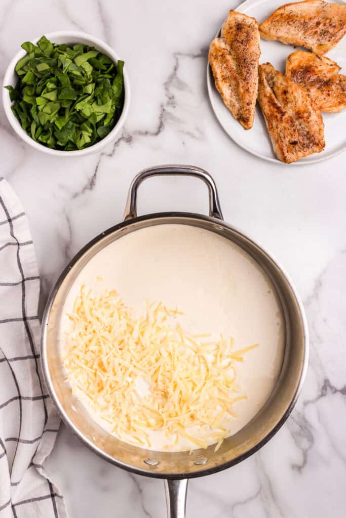 Shredded cheese added into the creamy sauce base in a skillet, ready to be melted for a rich consistency.
