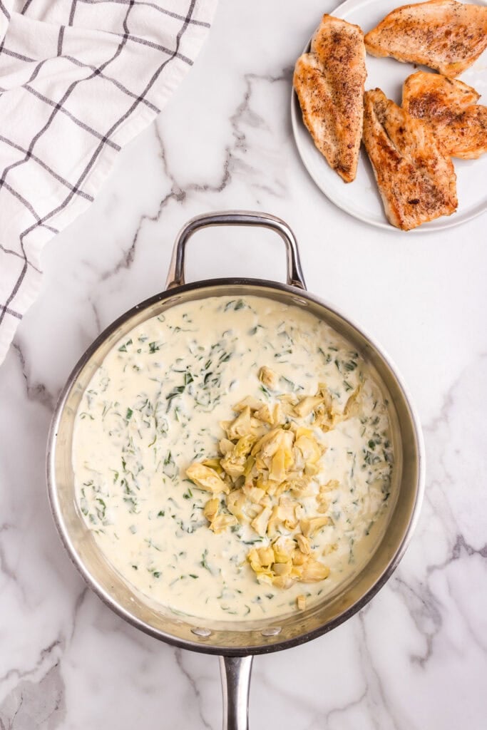 Chopped artichoke hearts added to the creamy spinach sauce in a skillet, just before mixing.