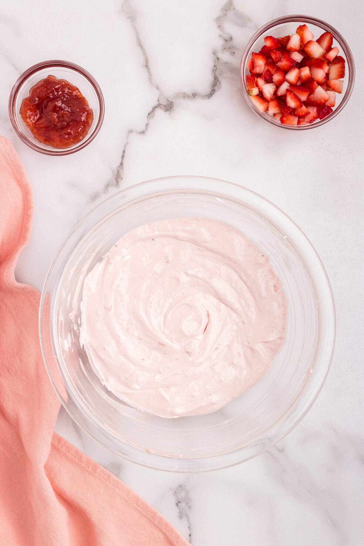 The strawberry dip mixture is fully blended into a smooth, light pink cream in a glass bowl, sitting on a marble countertop.