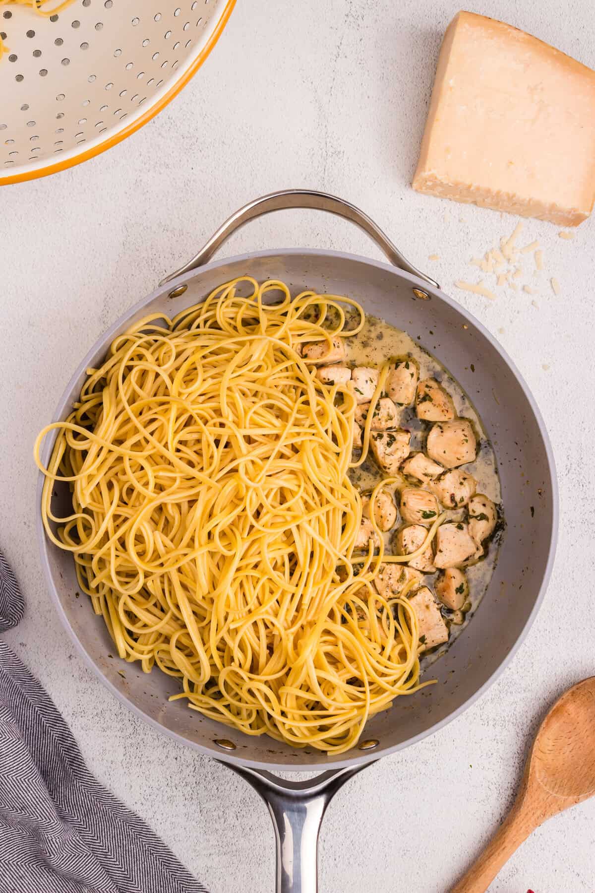 Cooked linguine pasta added to the skillet with the chicken and herb sauce, ready to be tossed together.