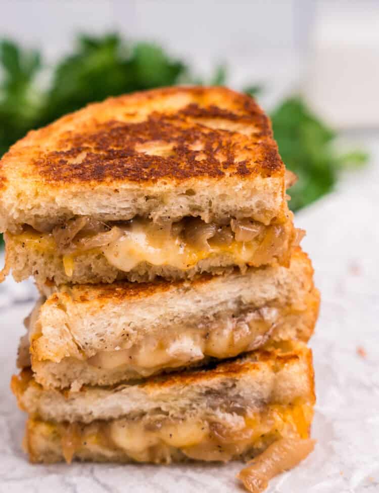 A close-up view of two stacked grilled cheese sandwiches. The bread is golden brown and crispy, with gooey, melted cheese and caramelized onions visible between the slices.