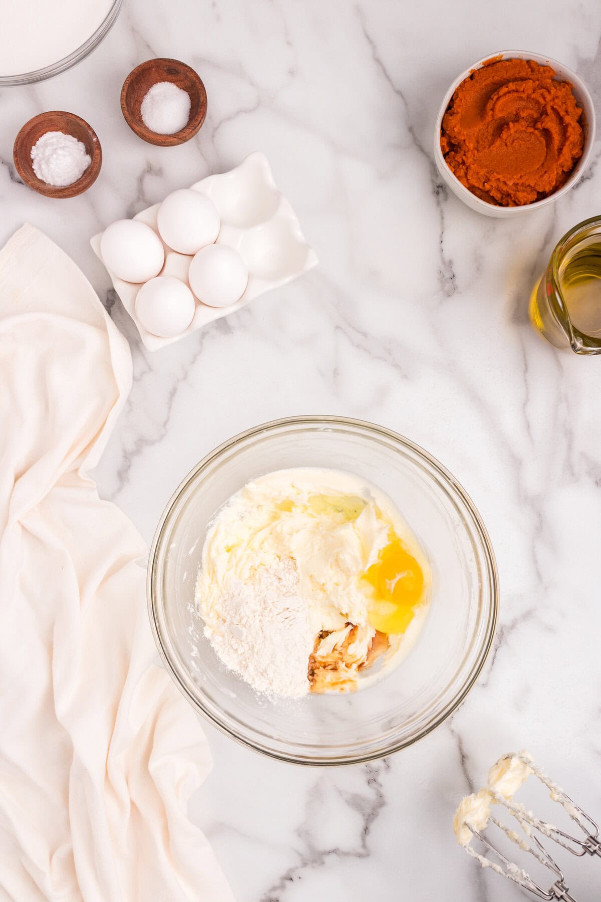 Glass bowl with cream cheese, flour, egg, and vanilla extract ready to be mixed together for the filling on a marble surface.