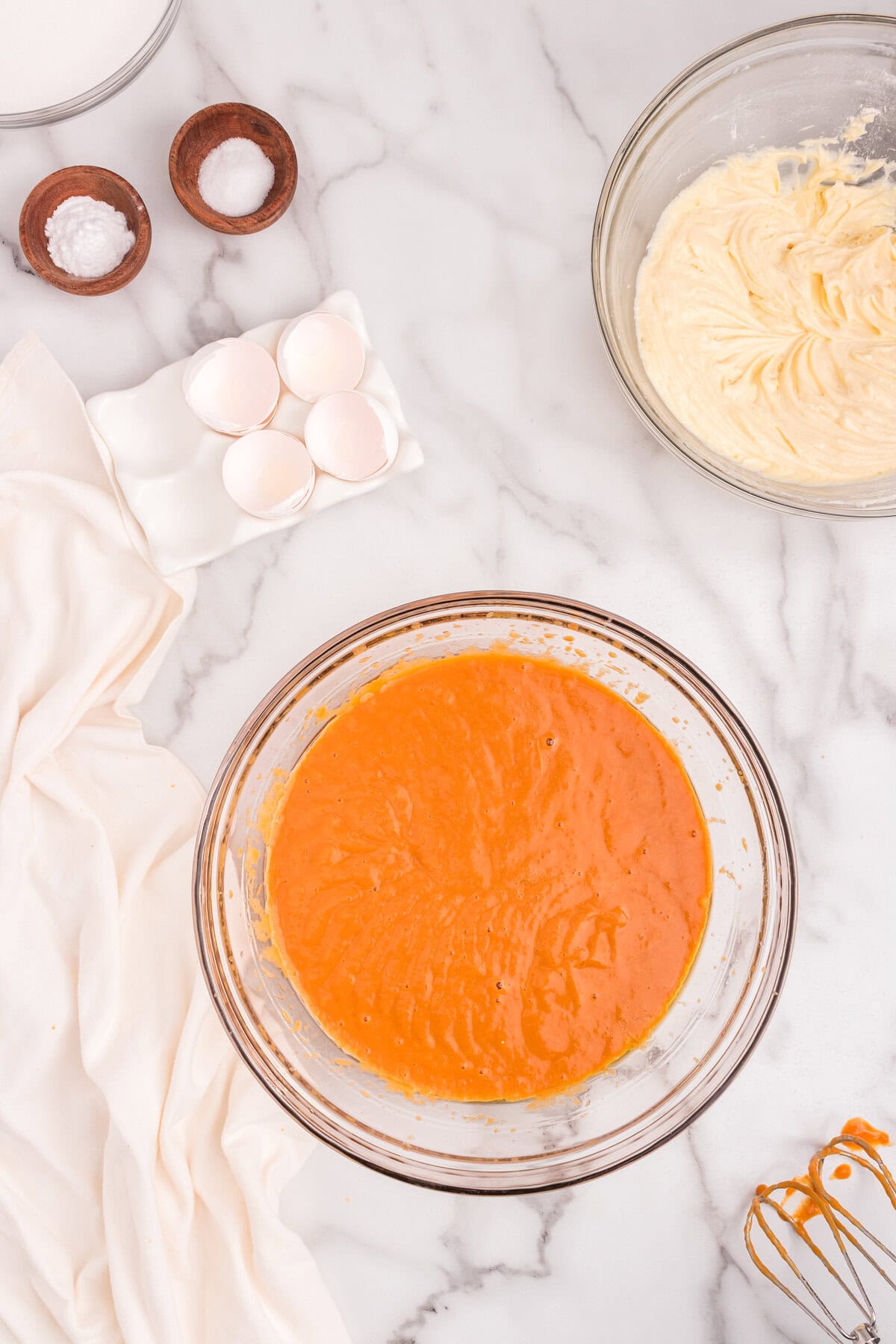 Pumpkin, oil, and eggs fully blended into a smooth orange mixture in a large glass mixing bowl