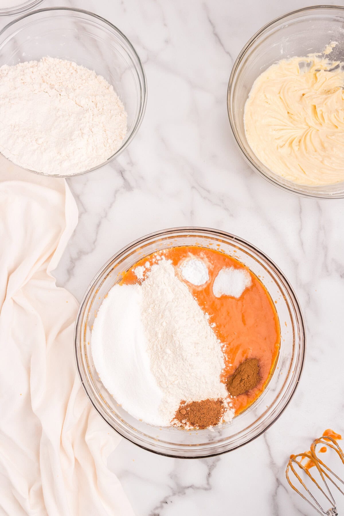 Pumpkin batter in a mixing bowl with flour, sugar, baking soda, salt, and spices piled on top, ready to be mixed into the final batter.