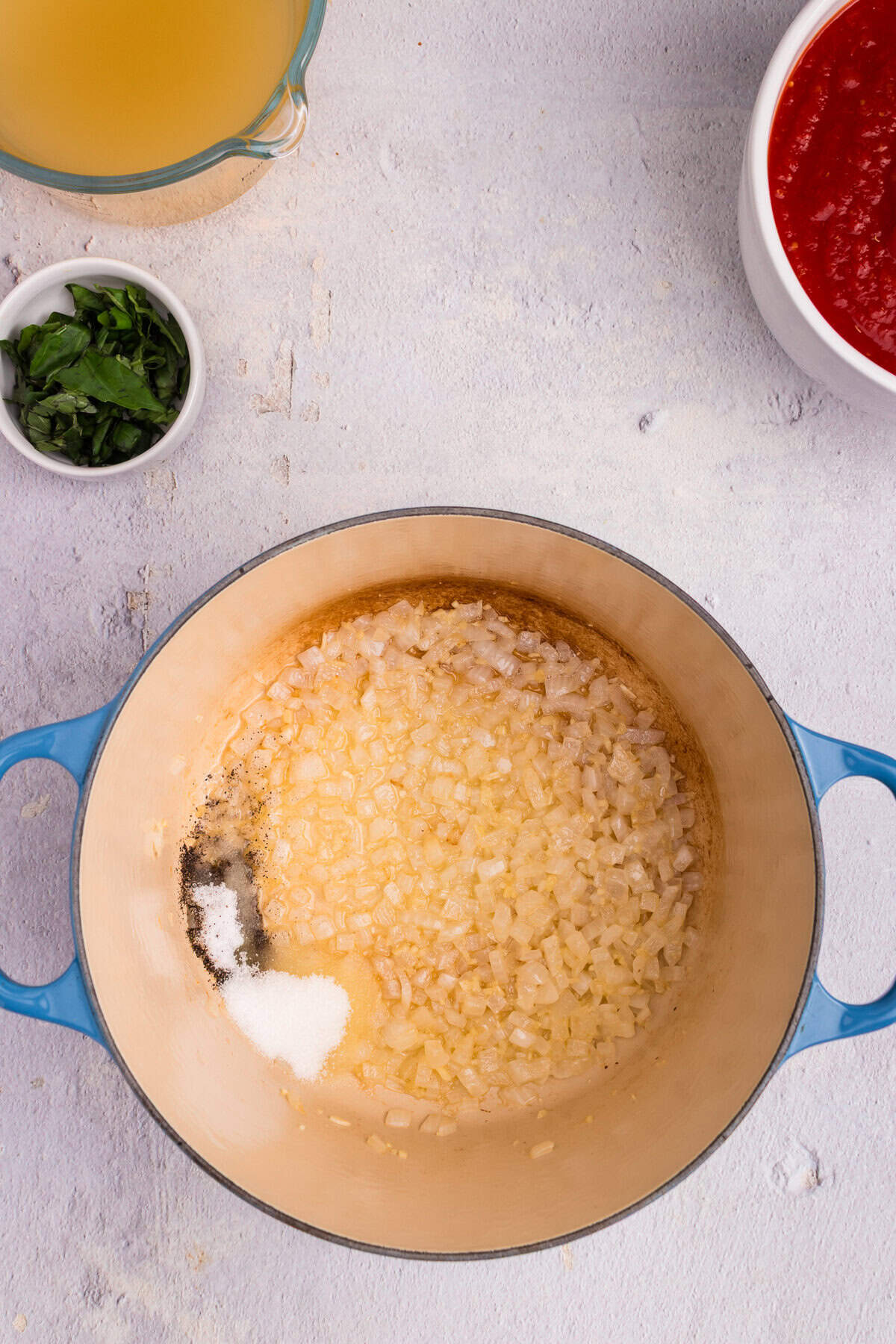 Salt and pepper added to the sautéed onions in the Dutch oven, with other ingredients still visible nearby.
