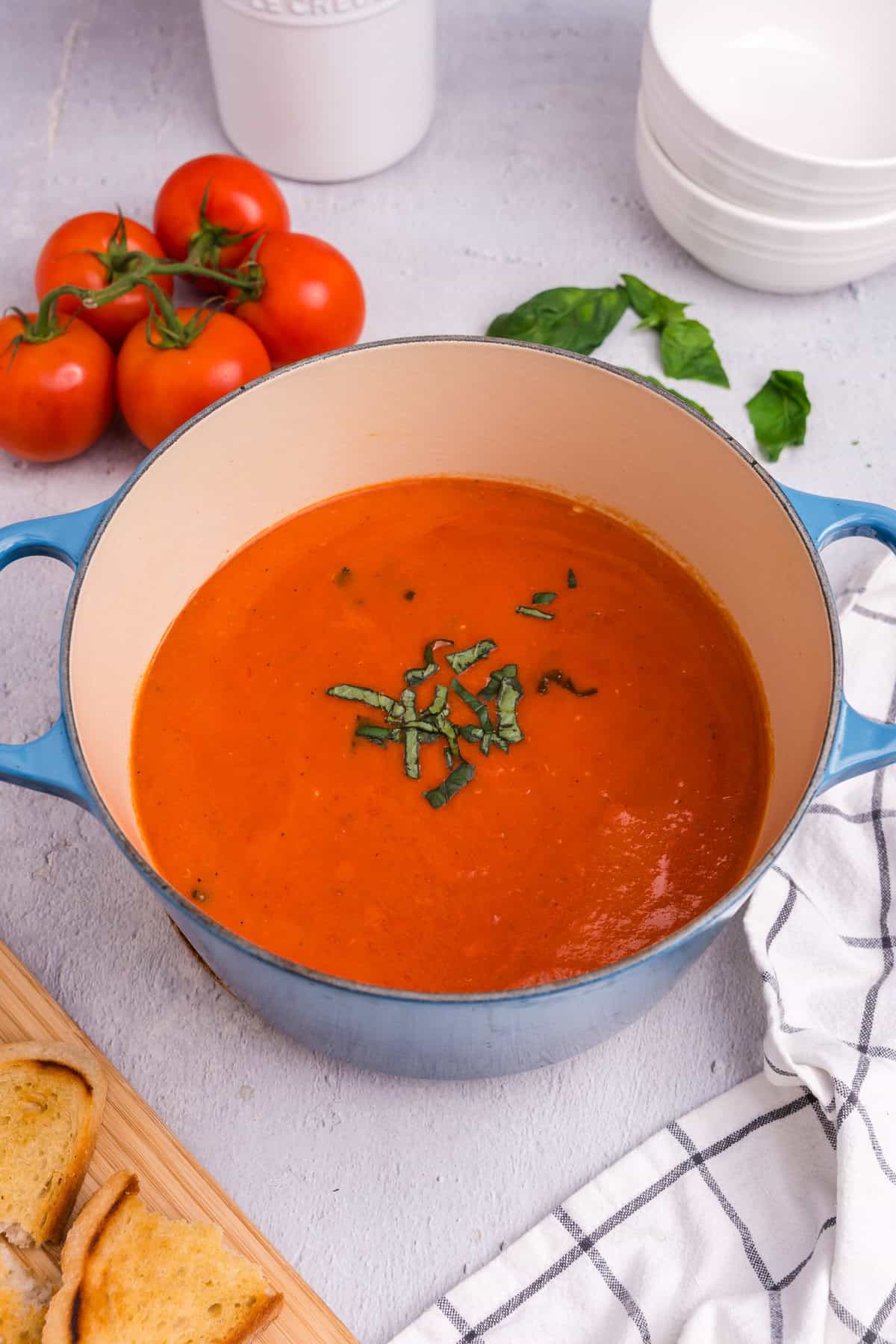 Garnished tomato soup in the Dutch oven with chopped basil on top, ready to be ladled out, accompanied by toasted bread.