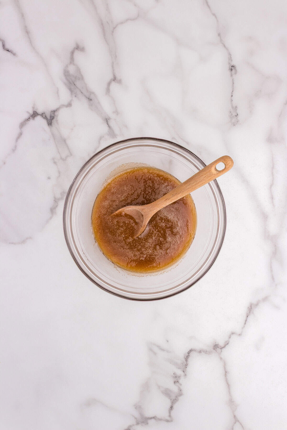 Brown sugar and maple syrup mixed together in a glass bowl with a wooden spoon.