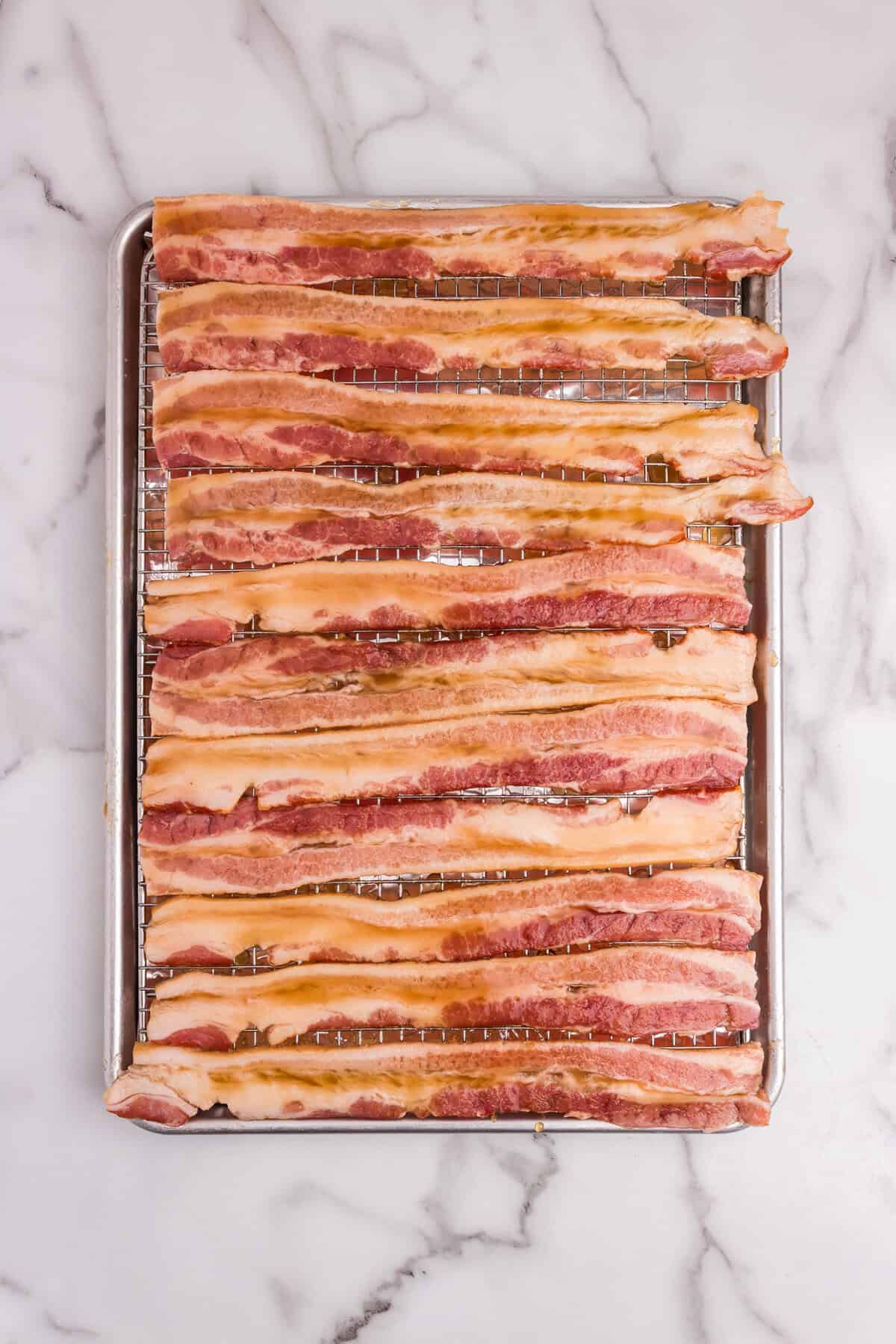 Raw bacon strips brushed with a shiny sugar and syrup glaze on a wire rack.