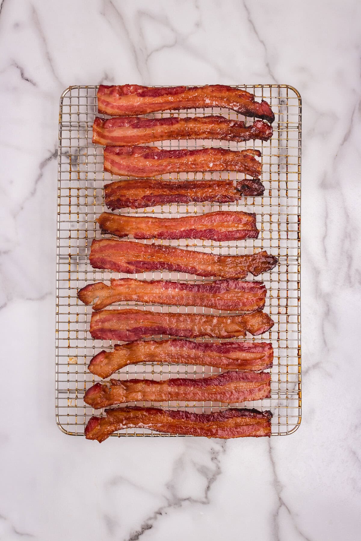 Fully baked candied bacon strips on a cooling rack, glistening with caramelized glaze.