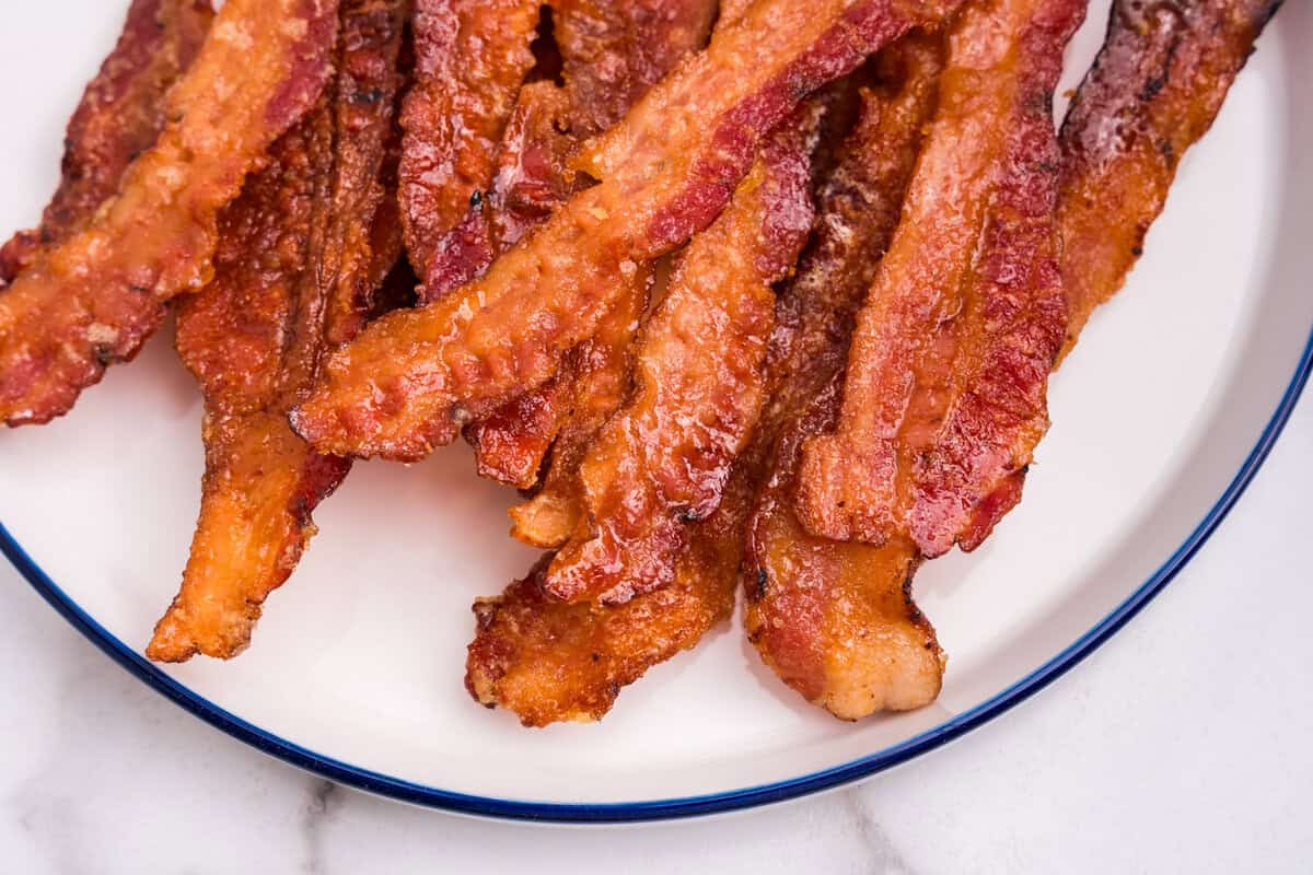 Plate of finished candied bacon piled together, crispy and coated in a shiny glaze.