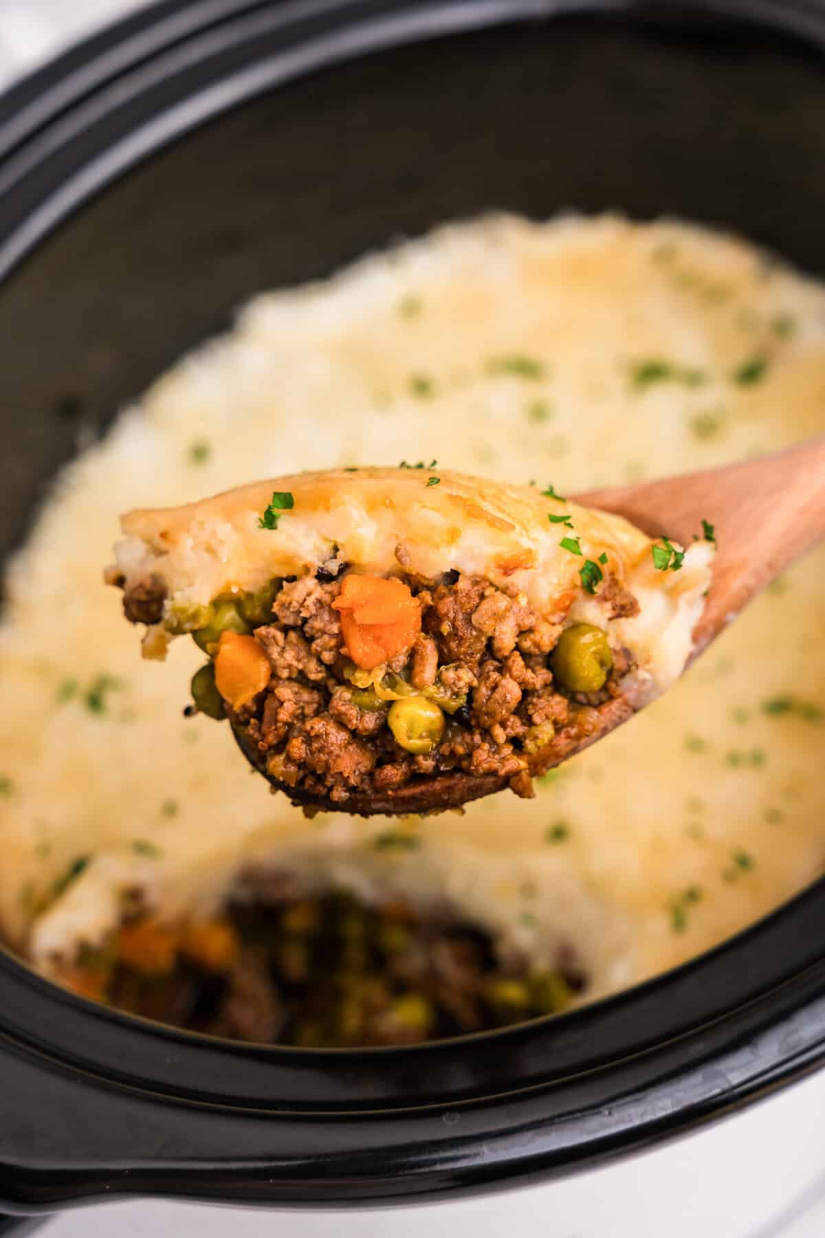 Partial view inside the slow cooker with a portion of shepherd’s pie scooped out, exposing the layers beneath the potato topping.

