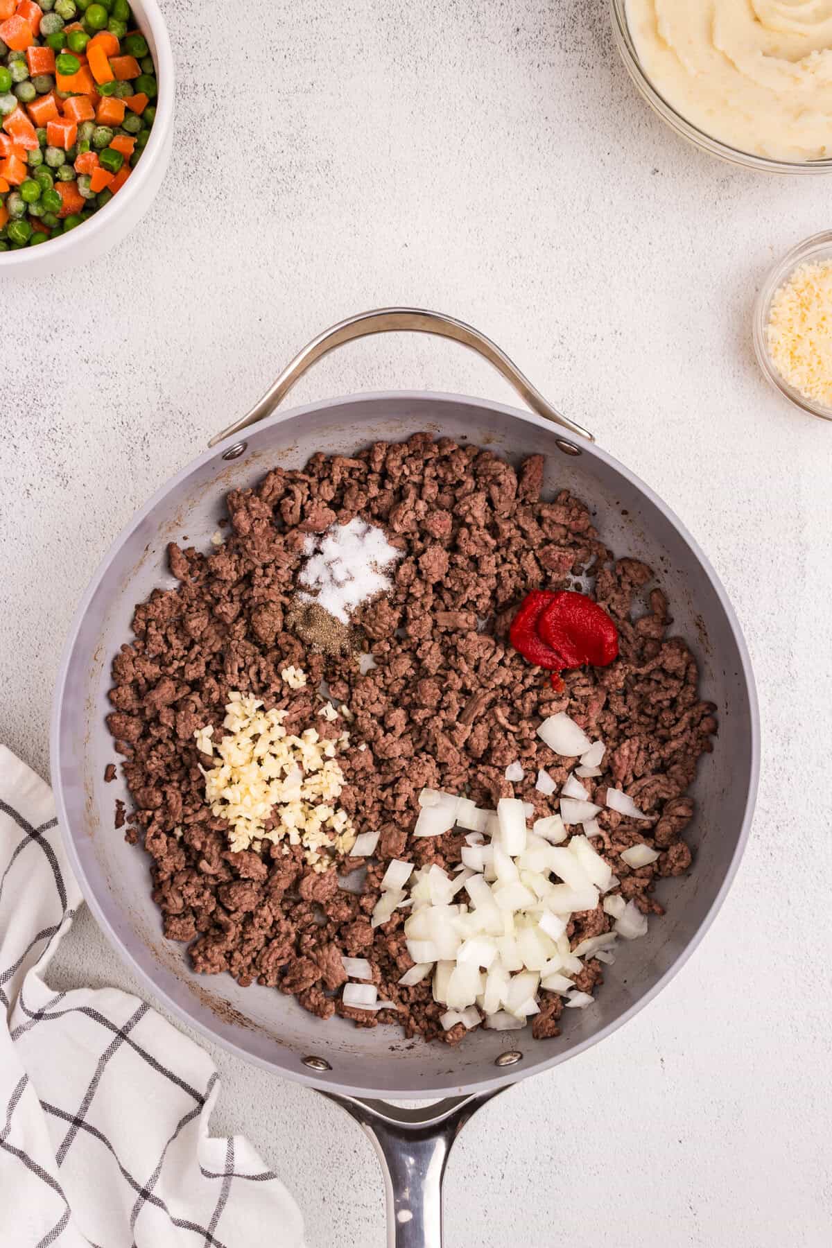 Raw ingredients in skillet with cooked ground beef. Includes diced onions, minced garlic, tomato paste, salt, and pepper.