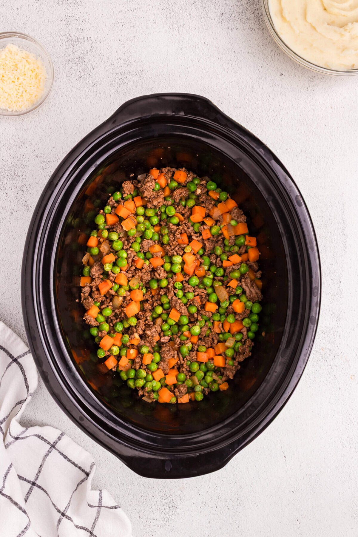Mixed ground beef and vegetables evenly distributed at the bottom of the slow cooker.