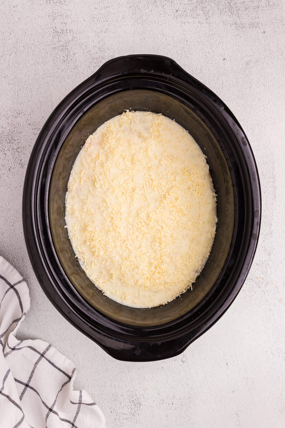 Mashed potatoes spread over the meat and vegetable mixture inside the slow cooker, topped with shredded cheese.