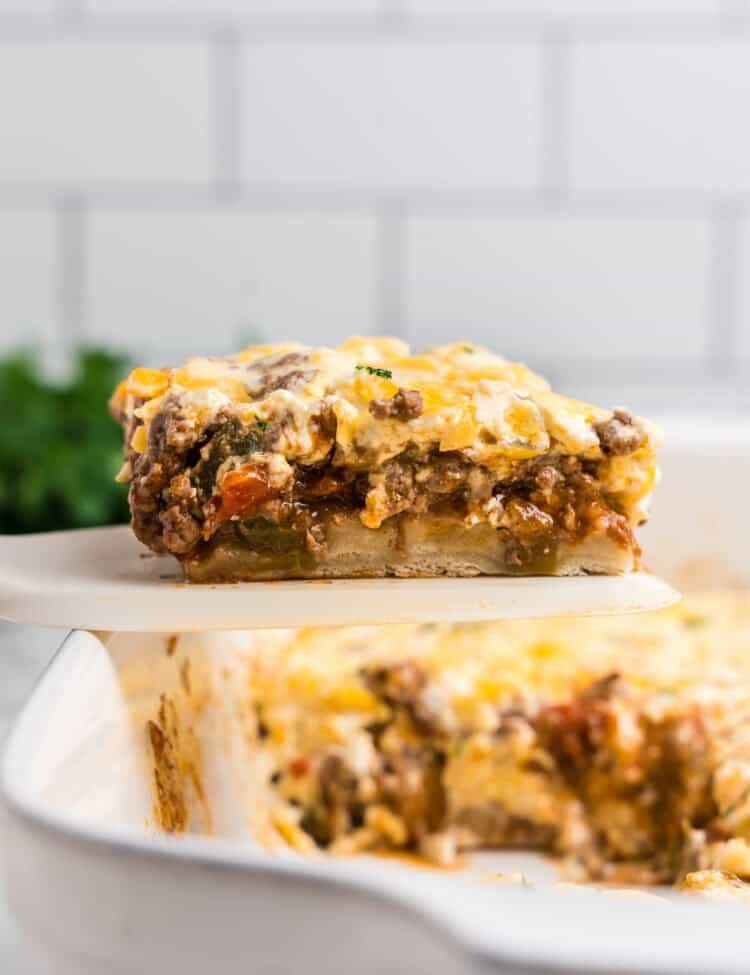 A slice of the casserole being lifted from the baking dish, revealing layers of ground beef, melted cheese, and a biscuit-like base.