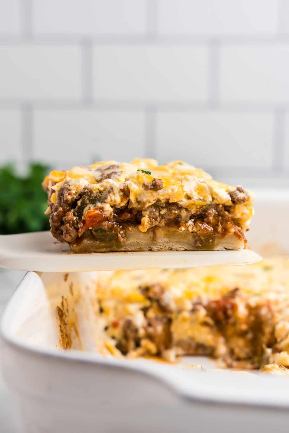 A slice of the casserole being lifted from the baking dish, revealing layers of ground beef, melted cheese, and a biscuit-like base.