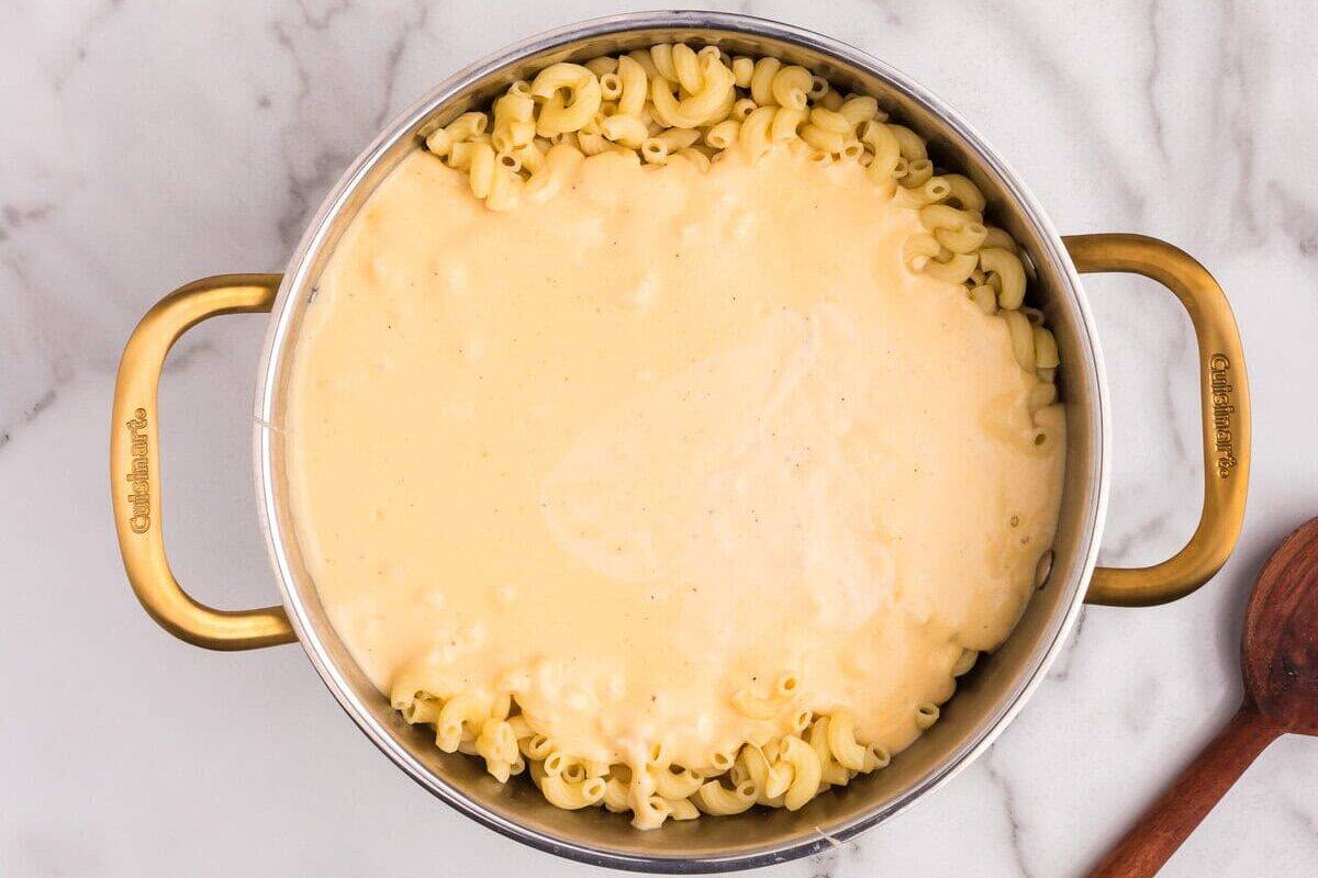 Overhead view of macaroni in a pot, now topped with the cheese sauce, with bowls of lobster meat and breadcrumb mixture nearby.